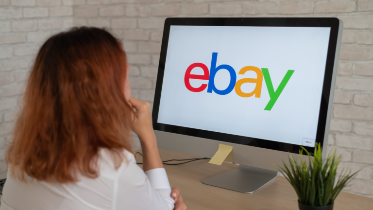 Une femme est assise en face d'un ordinateur affichant le logo d’eBay. Elle semble concentrée, illustrant le shopping en ligne, le e-commerce ou la vente sur marketplace.