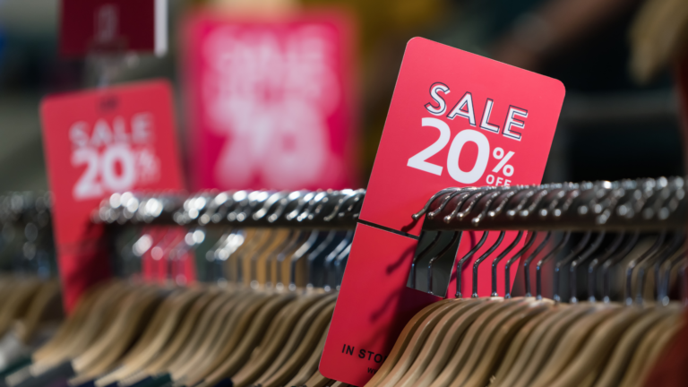 Un gros plan sur des cintres en magasin avec une étiquette rouge indiquant "SALE 20% OFF". L’image met en avant les promotions, les réductions et l’expérience d’achat en boutique.